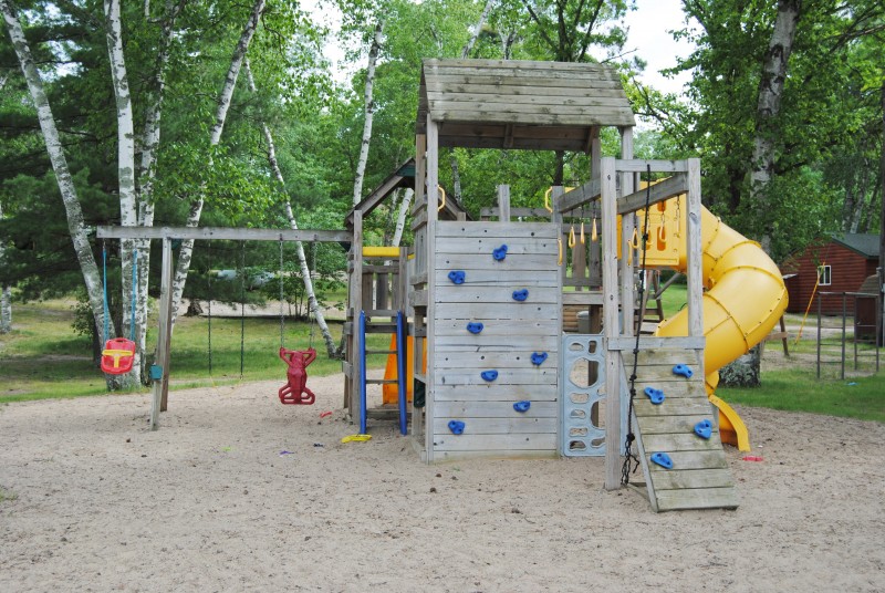 Wooden playground with climbing wall, slides, and swing set