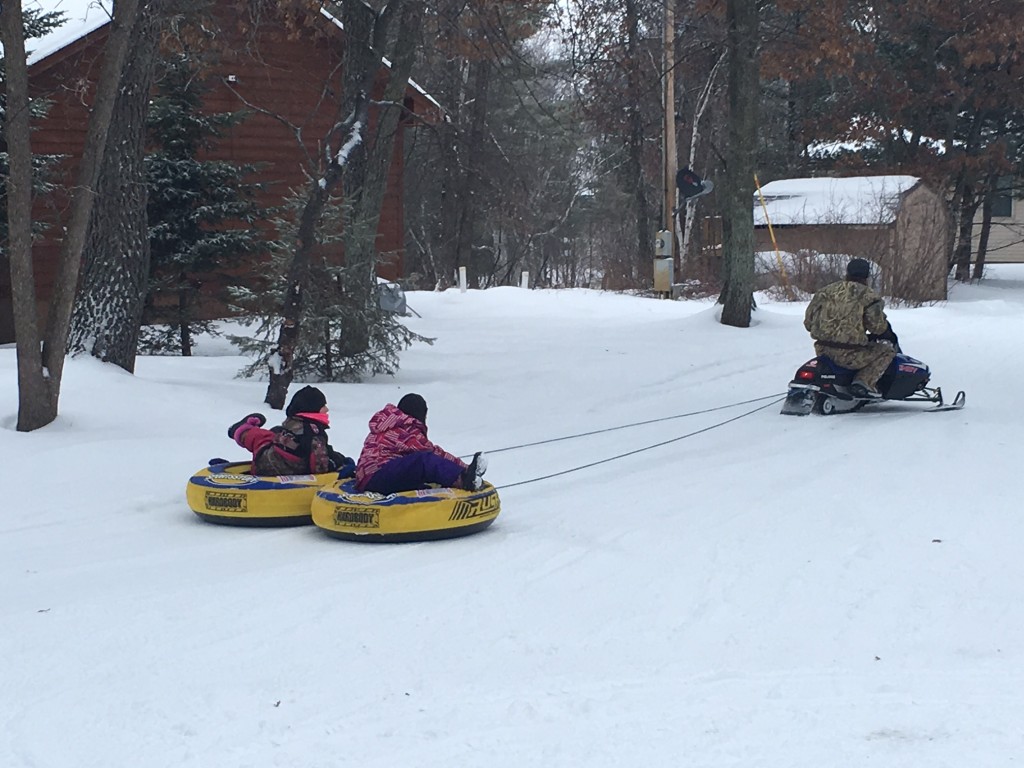Kids on sleds behind a snowmobile