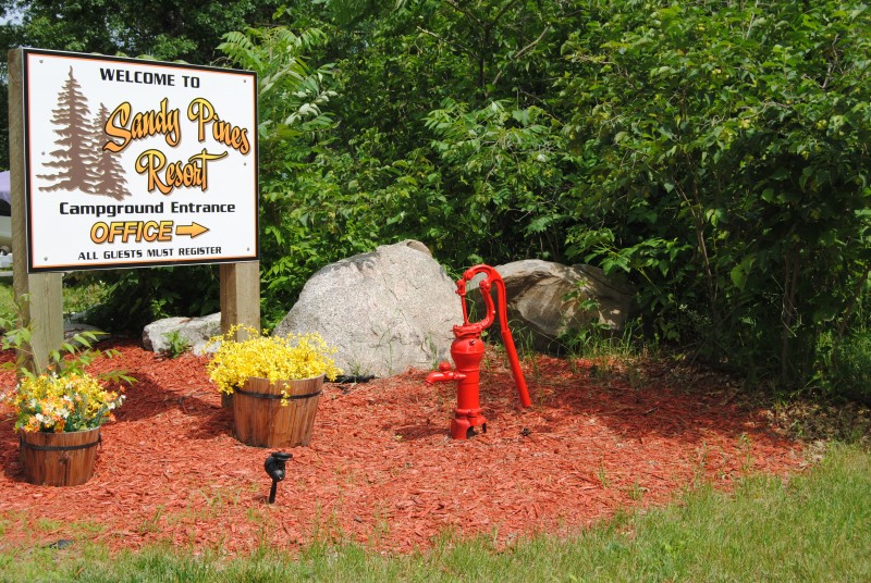 Sandy Pines Resort Campground Sign, water pump and flowers