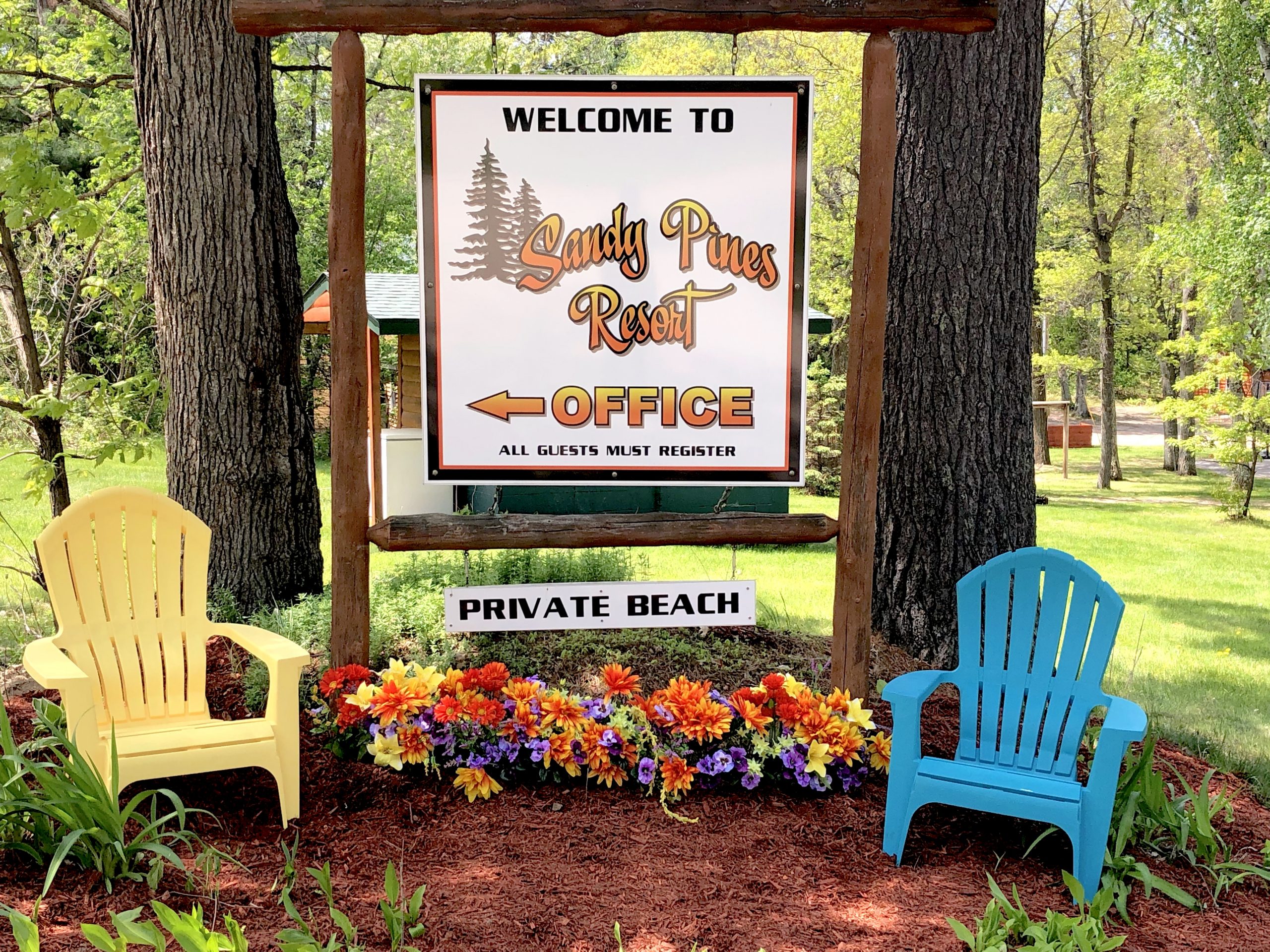 Sandy Pines Resort sign, Adirondack chairs, and flowers.